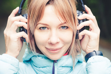 Close up Portrait of a beautiful young woman holding headphones listening to music outdoors in the forest. Joyful musicの写真素材