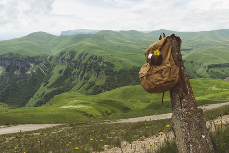 Hipster yellow vintage backpack with a mug fixed on it with a mug close-up front view. Travelers travel bag in the background of a mountain landscapeの写真素材