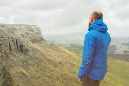bearded hipster tourist man standing on the edge of a rock and looking out into the distance on an epic plateau. The concept of tourismの写真素材
