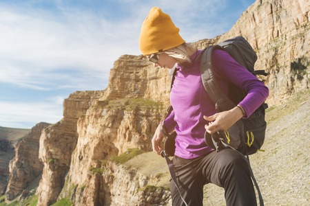 girl tourist in sunglasses puts a backpack on the nature on a background of epic rocks preparing for trekking with climbingの写真素材