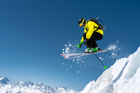 A skier in full sports equipment jumps into the precipice from the top of the glacier against the background of the blue sky and the Caucasian snow-capped mountains. Elbrus region. Russiaの写真素材