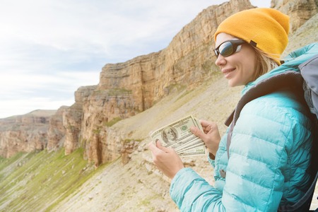 A traveler in a hat and sunglasses holds a hundred dollar bills in the hands of a fan against the...