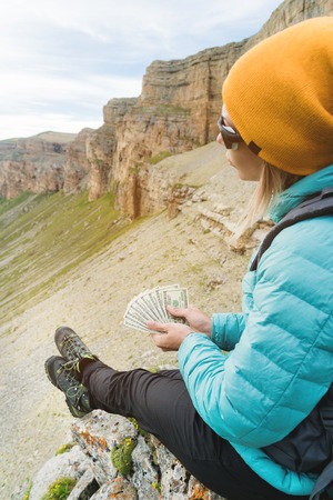 A traveler in a hat and sunglasses holds a hundred dollar bills in the hands of a fan against the...