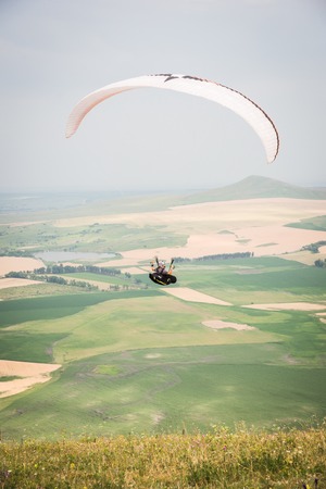 White orange paraglide with a paraglider in a cocoon against the background of fields of the sky and clouds. Paragliding Sportsの写真素材
