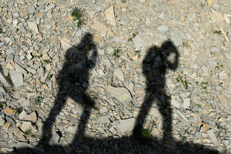 Two shadows of photographers on the earth going uphill. Silhouettes of two people walking uphillの写真素材
