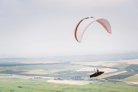 White orange paraglide with a paraglider in a cocoon against the background of fields of the sky and clouds. Paragliding Sportsの写真素材