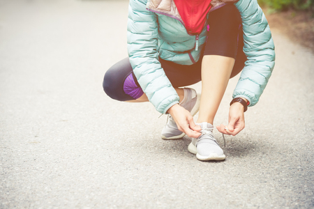 Girl runner tying laces for jogging her shoes on road in a park. Running shoes, Shoelaces. Exercise concept. Sport lifestyle. Vintage styleの写真素材