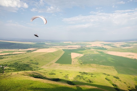 A white-orange paraglider flies over the mountainous terrainの写真素材