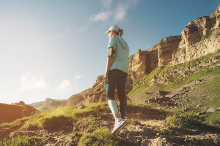 Attractive sports girl in a cap and headphones before jogging in a picturesque location next to the...