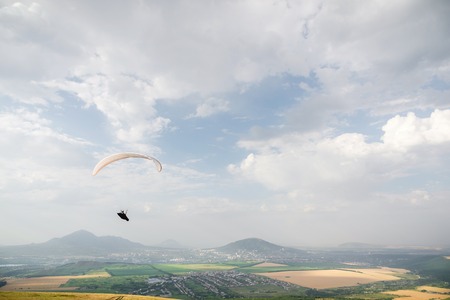 A white-orange paraglider flies over the mountainous terrainの写真素材