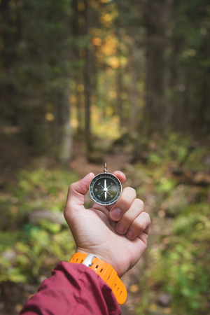 A beautiful male hand with a yellow watch strap holds a magnetic compass in the coniferous autumn forest. The concept of finding yourself the way and truthの写真素材