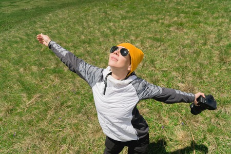 Happy girl photographer in sunglasses and with a camera in her hands throws her hands to the sky from the happiness of freedom in natureの写真素材