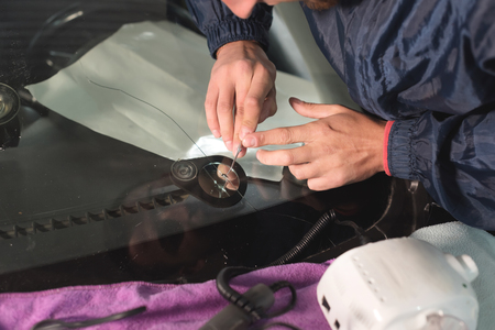 Close up Car glaze worker fixing and repairing a windshield or windshield of a car at a garage service station. Drill glass for repairの写真素材