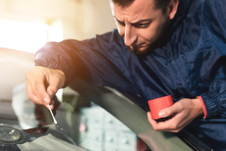 Close up Automobile glazier worker fixing and repair windscreen or windshield of a car in auto service station garageの写真素材