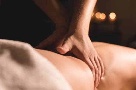 Close-up male hands doing healing massage with oil to a young girl in a dark cosmetology office. Dark keyの写真素材