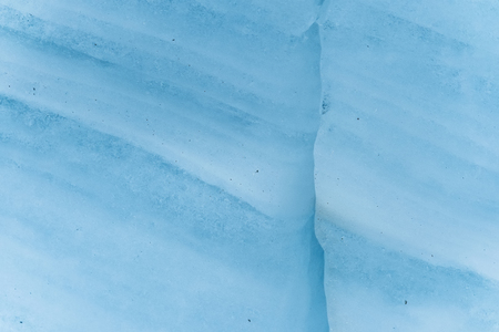 Close-up wall of a centuries-old glacier with a structure of stripes and bubbles. Ice blue light...