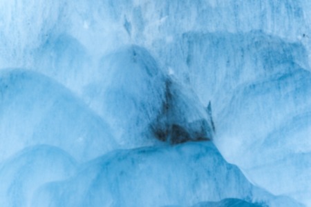 Close-up blurred wall of a centuries-old glacier with a structure of stripes and bubbles. Ice blue...