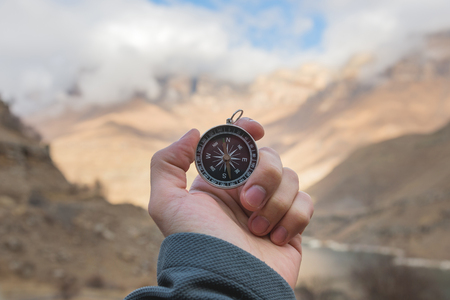A male Hiker is looking for a direction with a magnetic compass in the mountains in the fall. Point of view shot. Mans hand with a watch bracelet holds a compassの写真素材