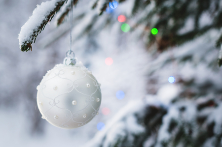 Close-up of a Christmas toy on a snow-covered lively tree in the winter forest on the background of lightsの写真素材