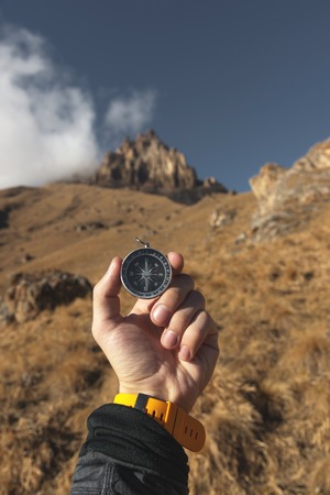 A male Hiker is looking for a direction with a magnetic compass in the mountains in the fall. Point of view shot. Mans hand with a watch bracelet holds a compassの写真素材