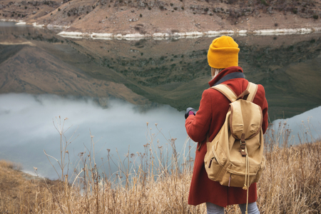 A portrait from the back of a girl photographer traveler on the background of a lake in the mountains in autumn or early spring. Travel conceptの写真素材