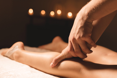 Close-up of male hands doing calf massage of female legs in a dark room with candles in the background. Cosmetology and spa treatmentsの写真素材