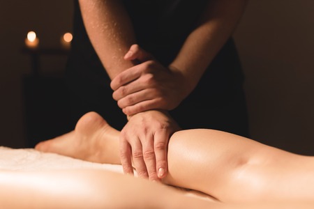 Close-up of male hands doing calf massage of female legs in a dark room with candles in the background. Cosmetology and spa treatmentsの写真素材