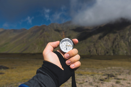 Viewpoint shot. A first-person view of a mans hand holds a compass against the background of an epic landscape with cliffs hills and a blue sky with cloudsの写真素材