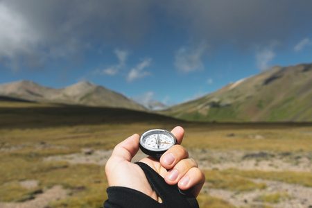 Viewpoint shot. A first-person view of a mans hand holds a compass against the background of an epic landscape with cliffs hills and a blue sky with cloudsの写真素材