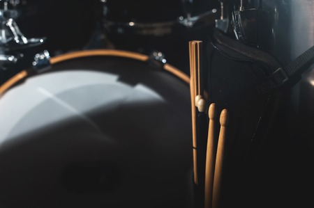 Closeup view of a drum set and Drumsticks in a dark studio. Black drum barrels with chrome trim. The concept of live performancesの写真素材