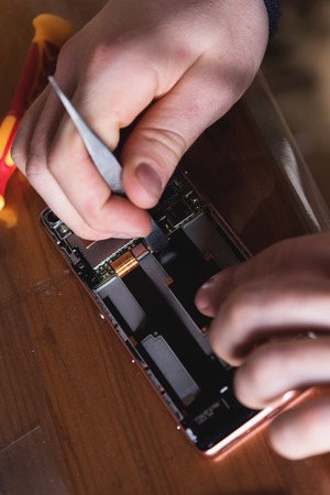 Close-up of the hand of a home craftsman repairing a disassembled smartphone. The concept of...