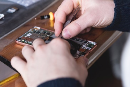 Close-up of the hand of a home craftsman repairing a disassembled smartphone. The concept of self-repair electronics at homeの写真素材