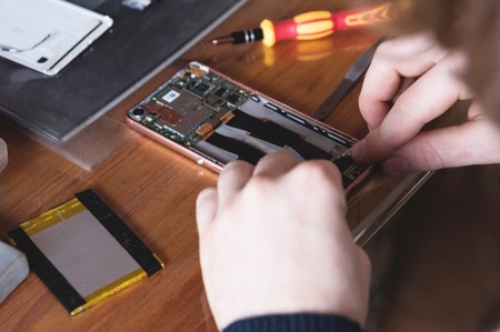 Close-up of the hand of a home craftsman repairing a disassembled smartphone. The concept of self-repair electronics at homeの写真素材