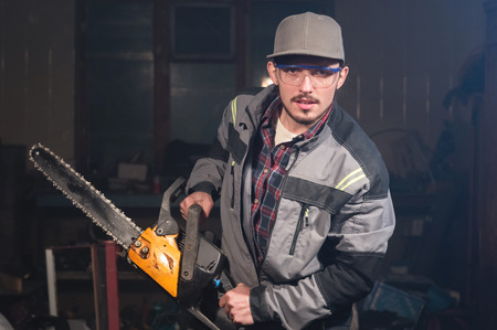 Portrait of a young carpenter holding in his hands a chainsaw threatening the viewer with threats. Security breach. Jokesの写真素材