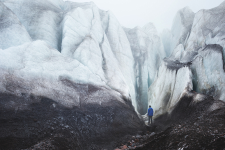 A climber with an ice ax stands at the foot of the Great Glacier next to an epic crack in the fog in the mountains. Insurmountable obstacleの写真素材