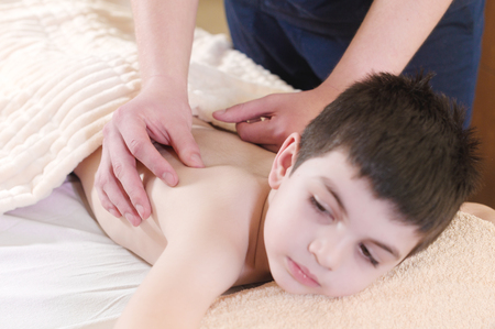 A little boy relaxes from a therapeutic massage. Male massage therapist makes a medical massage to the back of a childの写真素材