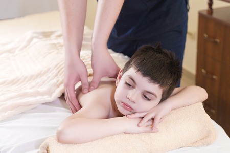 Relaxed little boy on reception at the chiropractor. Wellness massage procedureの写真素材