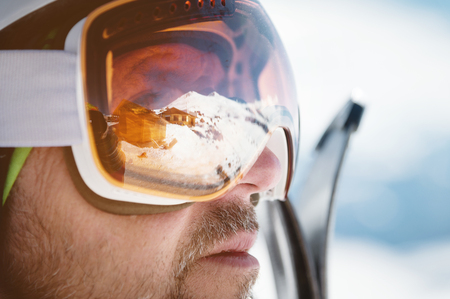 Close-up athlete skier in helmet and ski mask against the snow-capped mountains of a ski resort with a reflection of the Caucasian mountains in the maskの写真素材