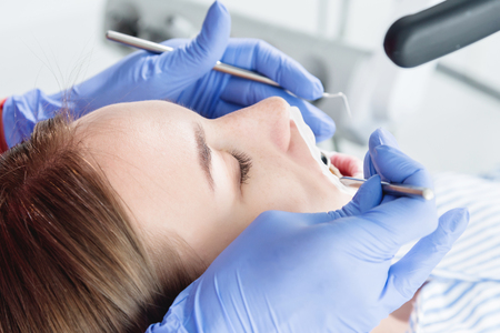 A close-up of the girls face is examined by a dental examiner with his mouth open and a napkin and eyes closed. Dentist hands with inspection toolsの写真素材
