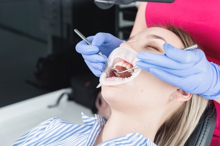 A close-up of the girls face is examined by a dental examiner with his mouth open and a napkin and...