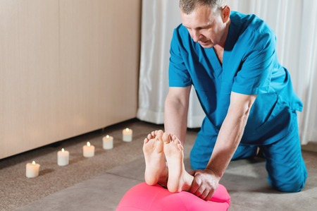 A male physiotherapist is stretching the knee joints to a young girl patient. Manual Wellness Therapyの写真素材