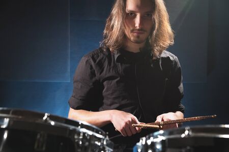 Portrait of a long-haired drummer with chopsticks in his hands sitting behind a drum set. Low key. Concepts of the creative freedom of the millenial generationの写真素材
