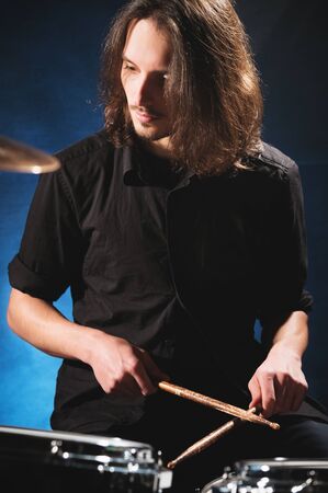 Portrait of a long-haired drummer with chopsticks in his hands sitting behind a drum set. Low key. Concepts of the creative freedom of the millenial generationの写真素材