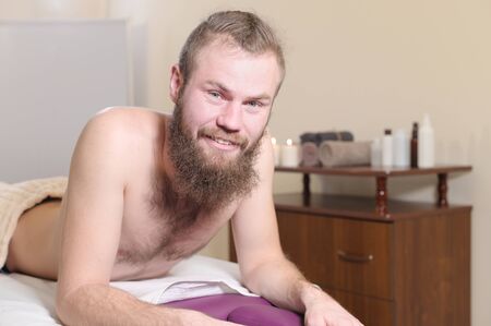 Smiling bearded man lying on a couch for manual therapy before a massageの写真素材