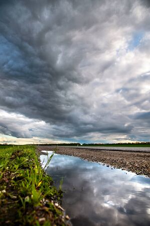 The reflection of the dramatic sky in a puddle on the side of a country road in the late evening...