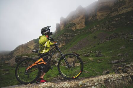 Side view of a man on a mountain bike standing on a rocky terrain and looking at a rock. The concept...