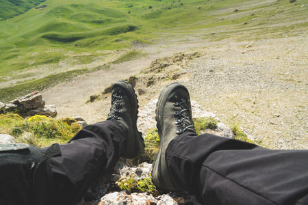 A first-person view POV of a man sits on the edge of a high cliff and enjoys the scenery. Wide angle human foot trekking rest. Tourism concept