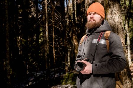 Portrait of a bearded photographer with a reflex camera in his hands in the winter coniferous forest. Photo travel conceptの写真素材