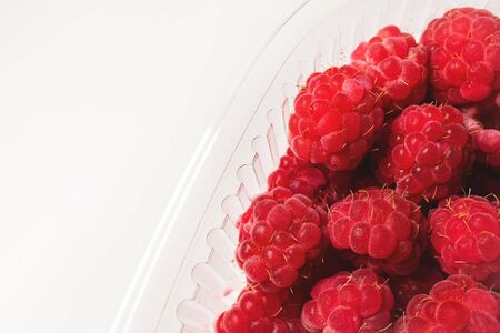 Close-up ripe juicy and delicious raspberry in a plastic transparent dish on a light background. Saturated healthy foodの写真素材