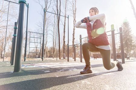 Portrait of a sports girl engaged in a workout in the winter on an outdoor sports field. Lunges and...